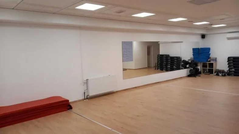 Großer Fitnessraum mit Holzboden, Wandspiegeln und Sportgeräten für verschiedene Übungen.