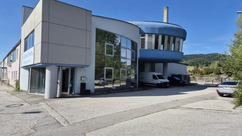 Modernes Geschäftsgebäude mit markanter runder Glasfassade und Parkplätzen im Freien.