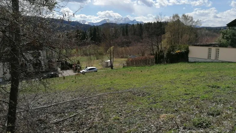 Grünes Grundstück mit weitem Blick auf eine Bergkette, Bäume und einige Gebäude in der Landschaft.