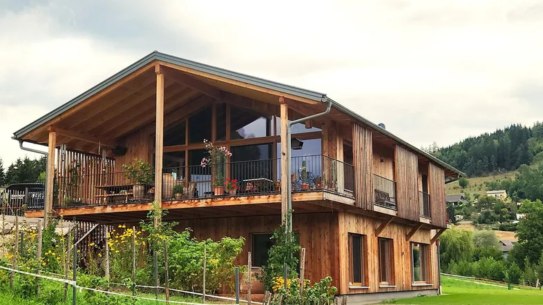 Modernes Holzhaus mit großem Balkon, großen Fenstern und umgebender Natur.