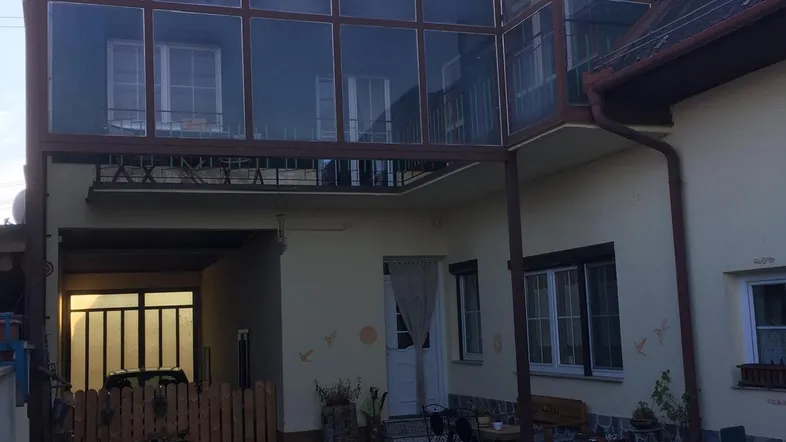 Außenansicht des Hauses mit einem verglasten Balkon oder Wintergarten und einem überdachten Eingangsbereich.