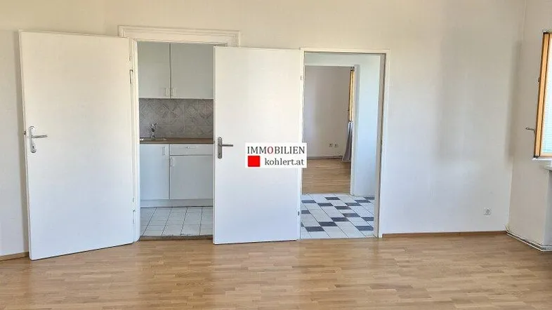Helles Wohnzimmer mit Parkettboden und Blick in die angrenzende Küche und einen weiteren Raum.