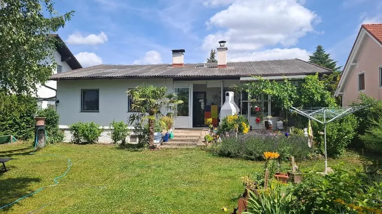 Blick auf das Haus von hinten mit einem gepflegten Garten und einer überdachten Terrasse.