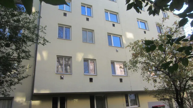 Mehrstöckiges Wohngebäude mit heller Fassade und Bäumen im Vordergrund, das einen gepflegten Eindruck macht.