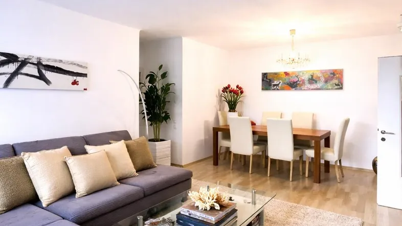 Helles Wohn- und Esszimmer mit modernem Sofa, Esstisch und Parkettboden.