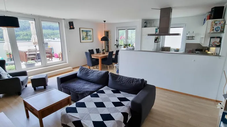 Heller offener Wohn- und Essbereich mit Zugang zu einem großen Balkon und Blick ins Grüne.