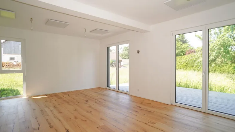 Helles Zimmer mit Holzboden und großen Schiebetüren zum Garten und zur Holzterrasse.