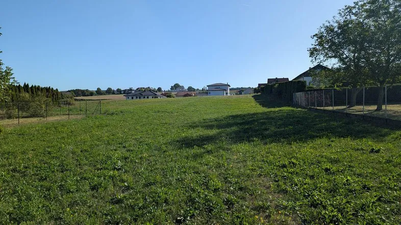 Weitläufiges grünes Grundstück mit Blick auf umliegende Häuser und offene Landschaft unter blauem Himmel.