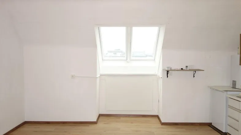 Helles Dachzimmer mit Dachfenster und integrierter Küchenzeile, ideal für ein Studio-Apartment.