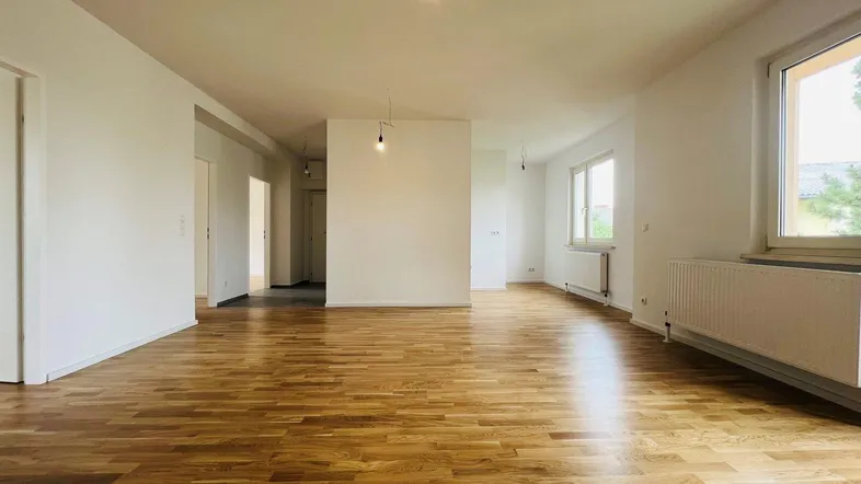 Helles, leeres Zimmer mit neuem Parkettboden und großen Fenstern, bereit zur individuellen Gestaltung.