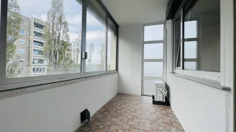 Verglaster Balkon mit Fliesenboden, Klimaanlage und Blick auf die umliegenden Gebäude.