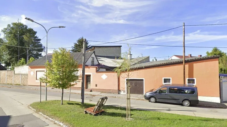 Ansicht des Hauses von der Straße mit orangefarbener Fassade und Garagentor unter blauem Himmel.