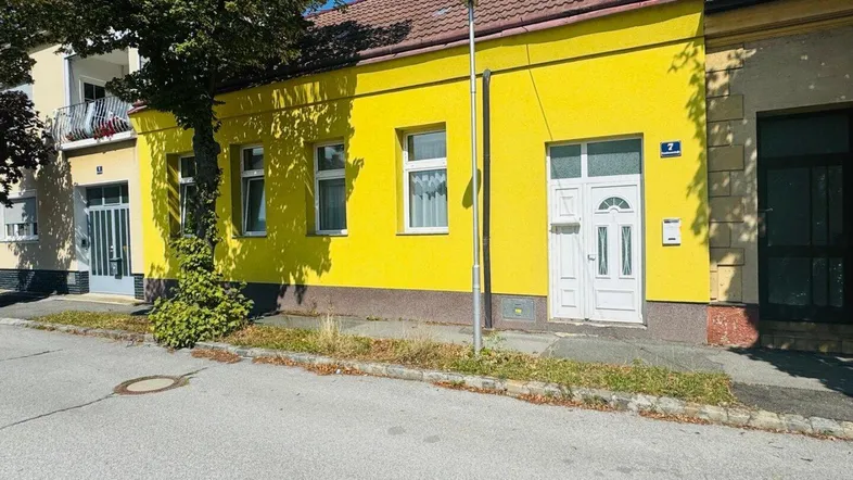 Gelbe Hausfassade mit weißen Fenstern und Haustür, direkt an einer ruhigen Straße gelegen.