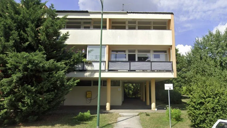 Mehrfamilienhaus mit Balkonen, umgeben von Grünflächen und Bäumen in einer Wohngegend.