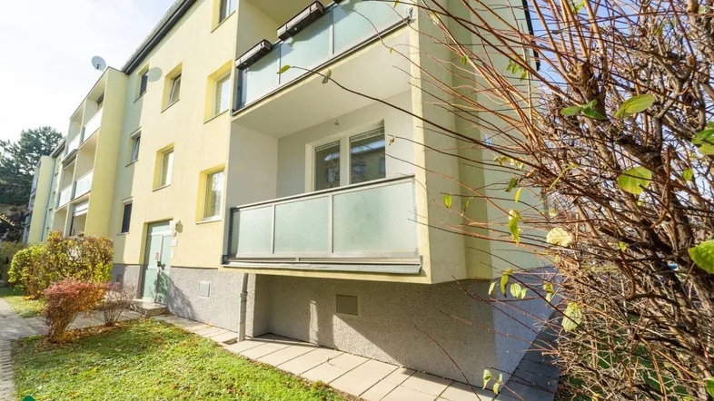 Gelbe Fassade eines Mehrfamilienhauses mit modernen Balkonen und Glasgeländern.