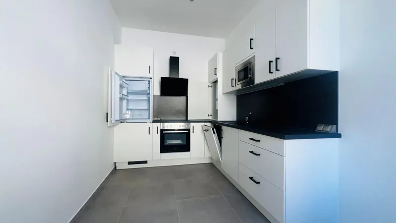 Moderne Einbauküche mit weißen Schränken, dunkler Arbeitsplatte und integrierten Geräten.