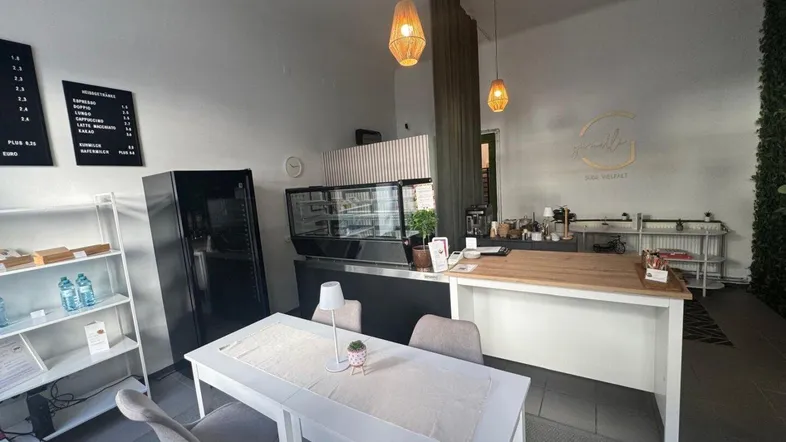 Moderne Café-Theke mit Sitzbereich, Speisekarte und dekorativer grüner Wand im Hintergrund.