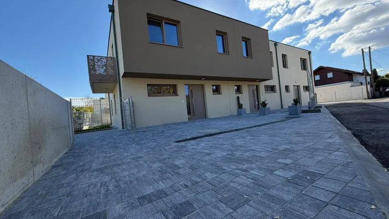 Moderne Reihenhäuser mit gepflastertem Vorplatz und zeitgenössischer Architektur unter blauem Himmel.