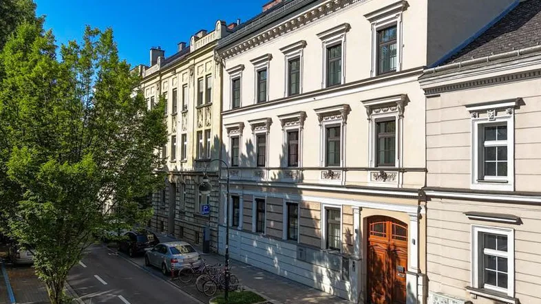 Historische Gebäudezeile an einer sonnigen Straße mit Bäumen und parkenden Autos.