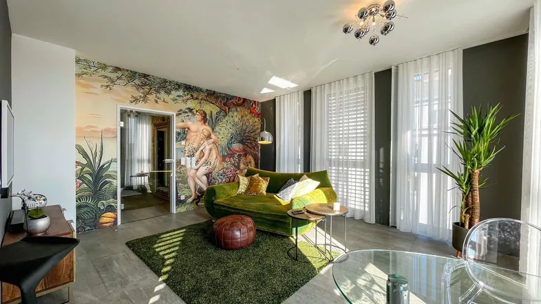 Helles Wohnzimmer mit auffälliger Wandtapete, grünem Sofa und modernen Möbeln.
