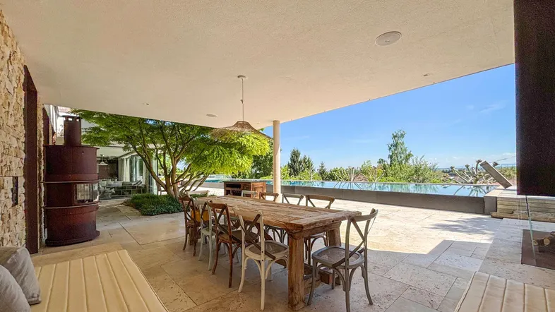 Geräumige überdachte Terrasse mit Esstisch, Kamin und Blick auf den Infinity-Pool und die Landschaft.
