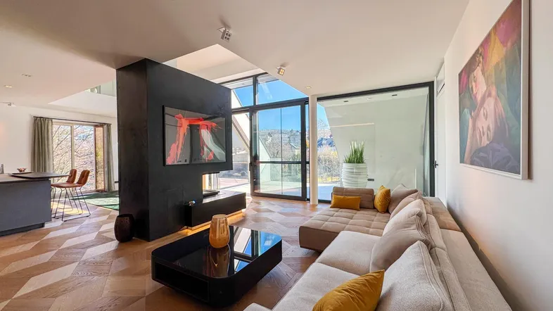 Helles, modernes Wohnzimmer mit Parkettboden, Kamin und großen Fensterfronten mit Bergblick.