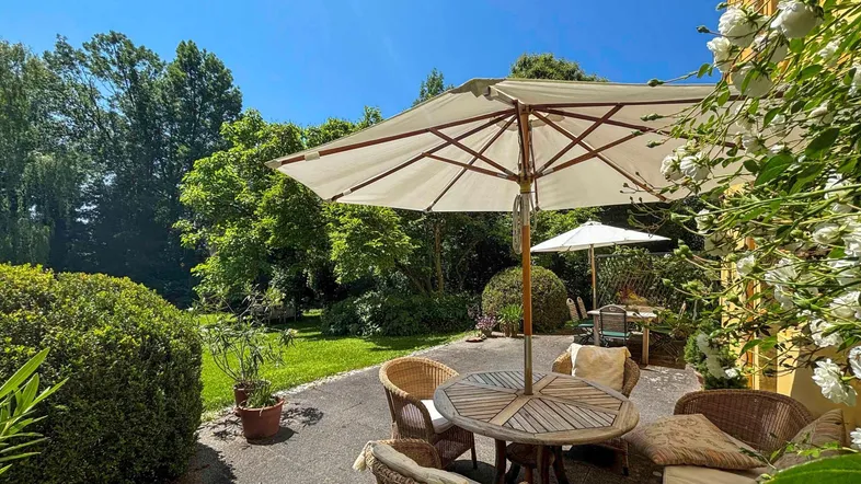 Gemütliche Terrasse mit Gartenmöbeln und Sonnenschirm, umgeben von üppigem Grün.