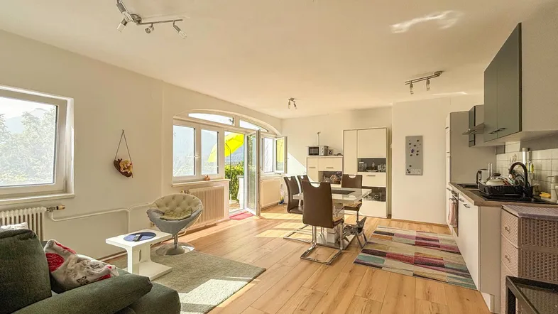 Helles, offenes Wohnzimmer mit Essbereich, integrierter Küche und Zugang zum Balkon.