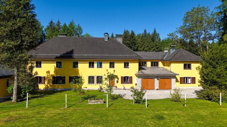 Großzügiges Anwesen mit gelber Fassade, umgeben von viel Grün und Bäumen.