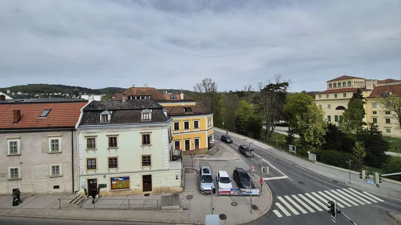 Blick auf eine belebte Straße mit historischen Gebäuden und einer weiten Landschaft im Hintergrund.