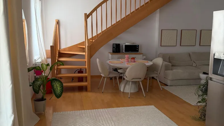 Heller offener Wohn- und Essbereich mit Holztreppe, Holzboden und modernem Teppich.