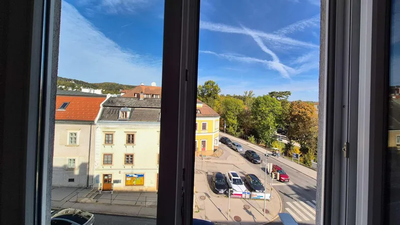 Blick aus dem Fenster auf die belebte Straße mit parkenden Autos und historischen Gebäuden unter blauem Himmel.