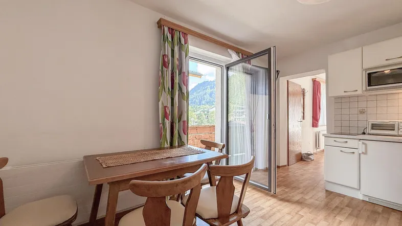 Helle Küche mit Essbereich, Holztisch und Zugang zum Balkon mit Bergblick.