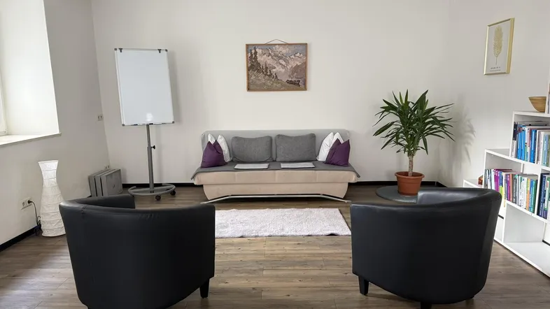 Heller Büroraum mit bequemer Couch, zwei Sesseln und einem Whiteboard für Besprechungen.