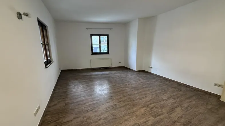 Heller, leerer Raum mit Laminatboden und zwei Fenstern, bereit zur individuellen Gestaltung.