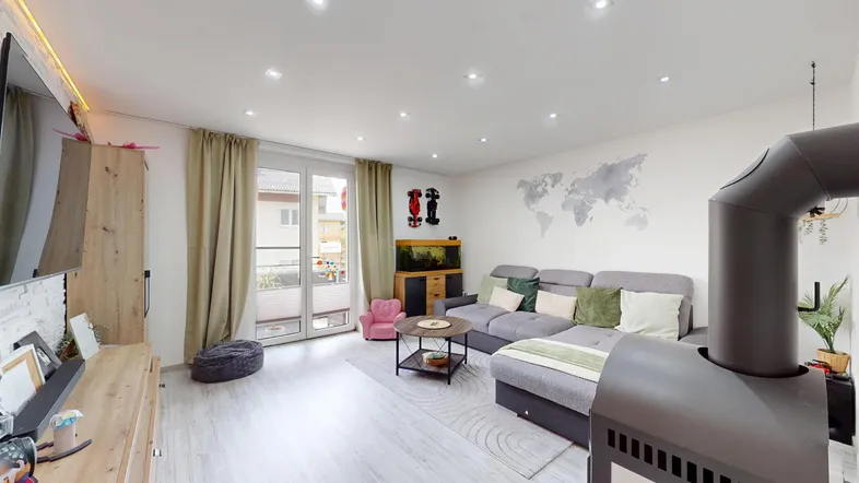Helles Wohnzimmer mit Zugang zum Balkon, bequemer Sitzecke und Kaminofen.