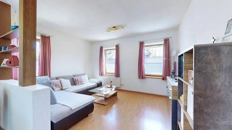 Helles Wohnzimmer mit beigem Sofa, Holzfußboden und Blick nach draußen durch die Fenster.