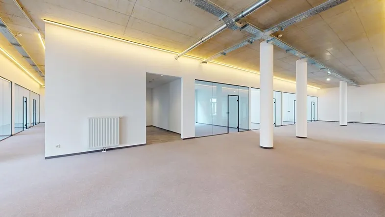 Geräumiges, modernes Büro mit Teppichboden, Glaswänden und sichtbaren Deckeninstallationen.