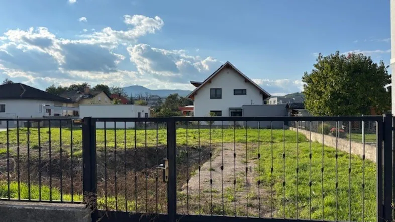 Grundstück mit Blick auf ein Einfamilienhaus, grüne Wiesen und eine bergige Landschaft im Hintergrund.