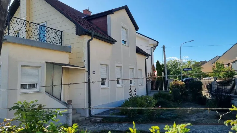 Helles Einfamilienhaus mit Balkon und Rollläden, umgeben von einem kleinen Vorgarten.