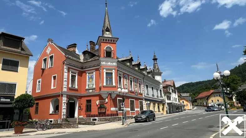 Historisches Gebäude mit markantem Turm und kunstvollen Fassadenmalereien an einer belebten Straße.
