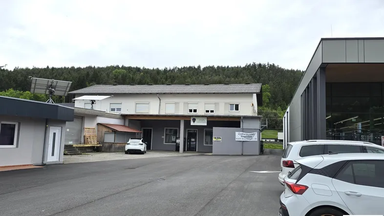 Ansicht des Gebäudes von außen mit Parkplatz, Photovoltaikanlage und umliegender Natur.