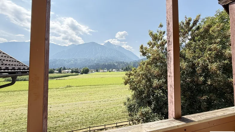Balkon mit Holzelementen und weitem Blick auf grüne Felder und majestätische Berge.