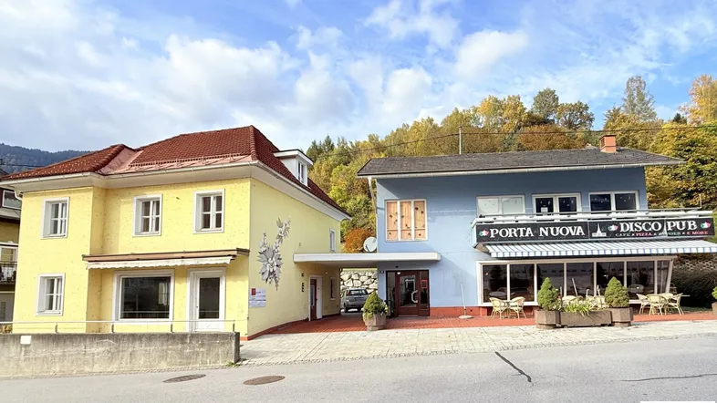 Ansicht von zwei Gebäuden, eines gelb und eines blau, mit einer Straße davor und Bäumen im Hintergrund.