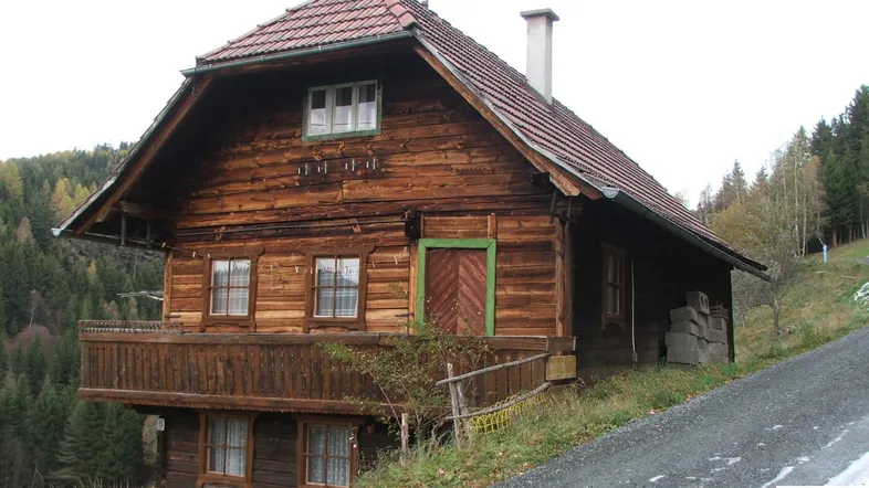 Rustikales Holzhaus mit Balkon und traditionellem Ziegeldach in bergiger Landschaft.
