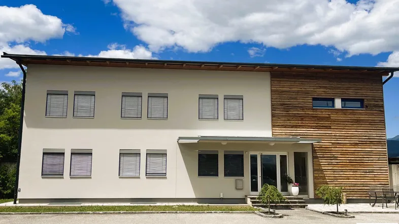 Modernes Gebäude mit heller Fassade und Holzverkleidung unter blauem Himmel und Wolken.