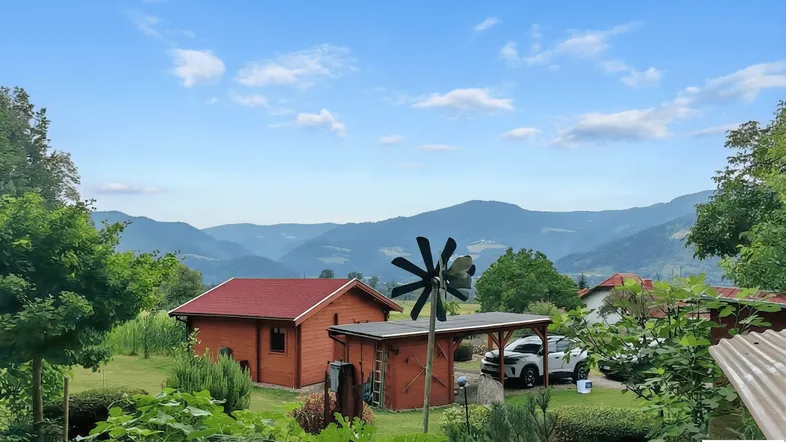 Blick auf ein charmantes Holzhaus mit rotem Dach, Carport und einer malerischen Bergkulisse im Hintergrund.