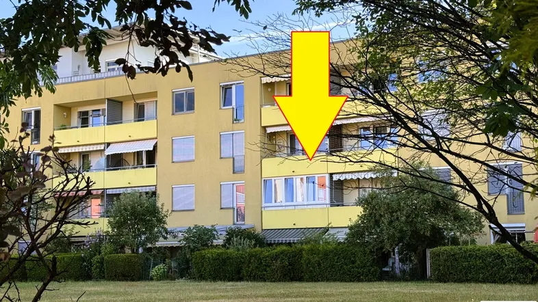 Gelbes Mehrfamilienhaus mit Balkonen und grüner Rasenfläche im Vordergrund.