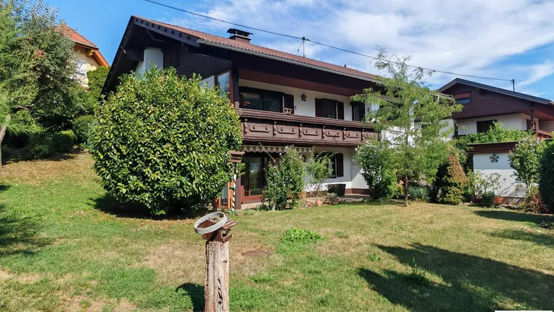 Traditionelles Haus mit gepflegtem Garten und üppiger Bepflanzung unter blauem Himmel.