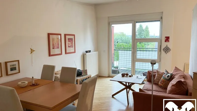 Heller Wohn- und Essbereich mit Holzboden, Zugang zum Balkon und Blick ins Grüne.